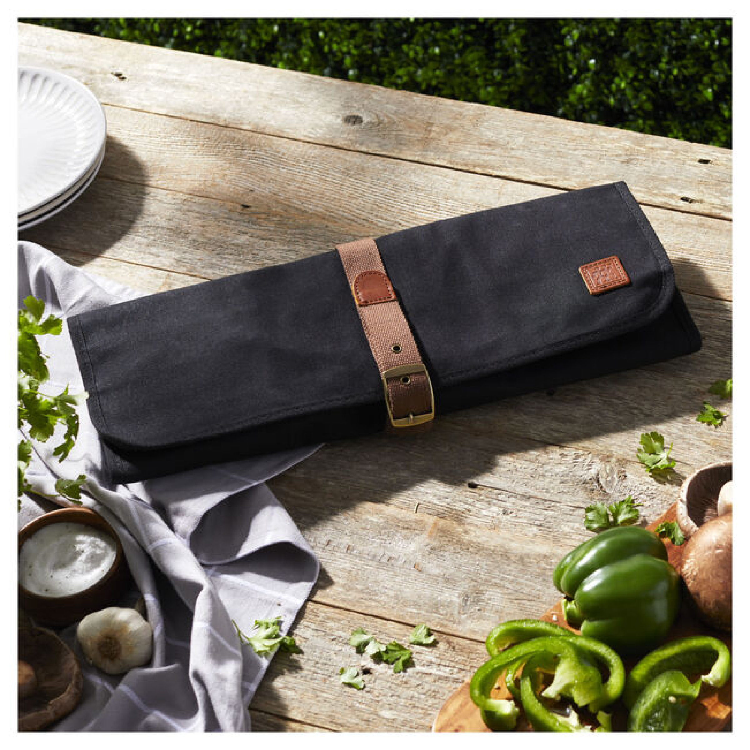 Black fabric grill tool roll with brown leather strap on tabletop