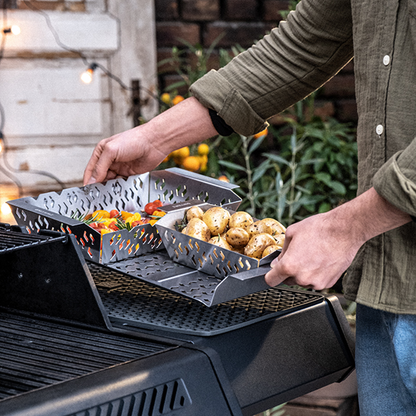 Perforated stainless grill basket set being placed on a barbecue grill