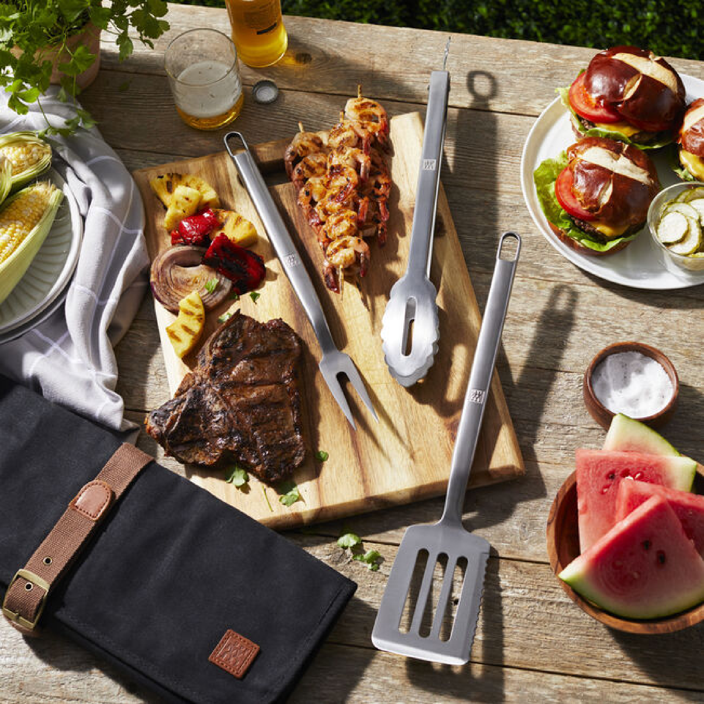 Stainless grill tools with black fabric tool roll and brown leather strap